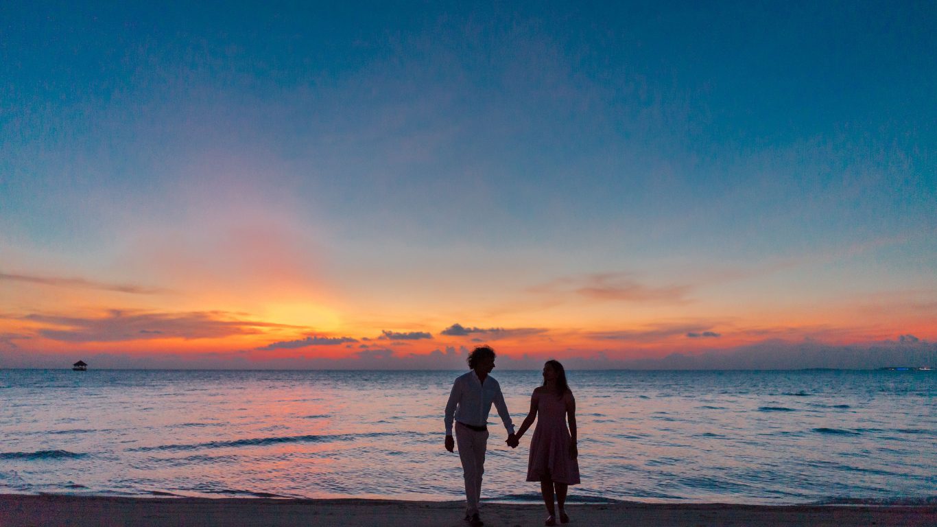 Couple walking hand in hand on the beach at sunset